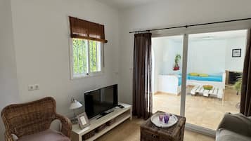 Una sala de estar con televisión, mobiliario de mimbre, una puerta corrediza de vidrio a un balcón y una ventana con vistas.