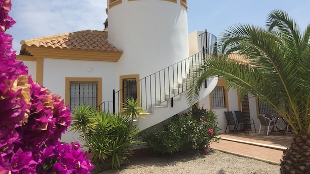 A white building with a tower, a staircase, and a patio area with chairs and plants.