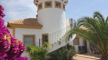 Un edificio blanco con una torre, una escalera y un patio con sillas y plantas.