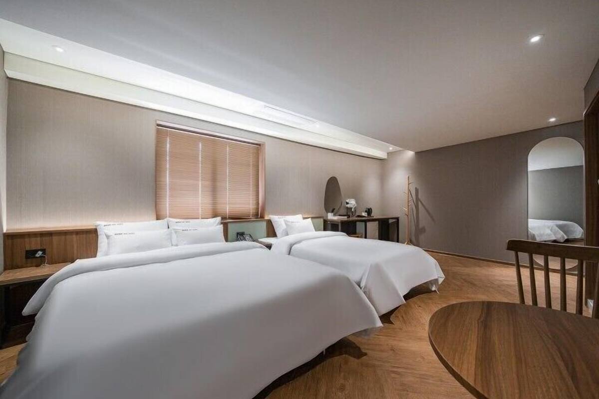 A modern hotel room with two beds, a desk, a chair, and a large mirror.