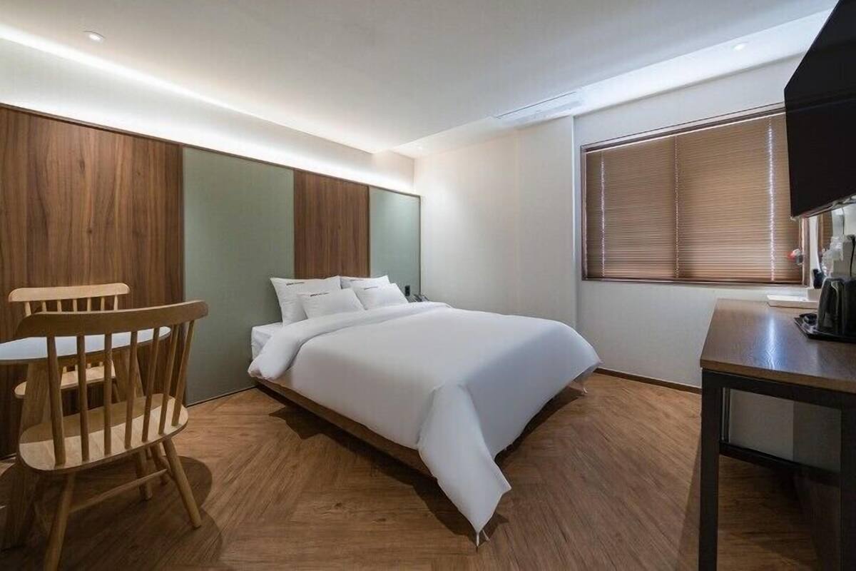 A modern hotel room with a large bed, wooden flooring, a desk, and a TV.