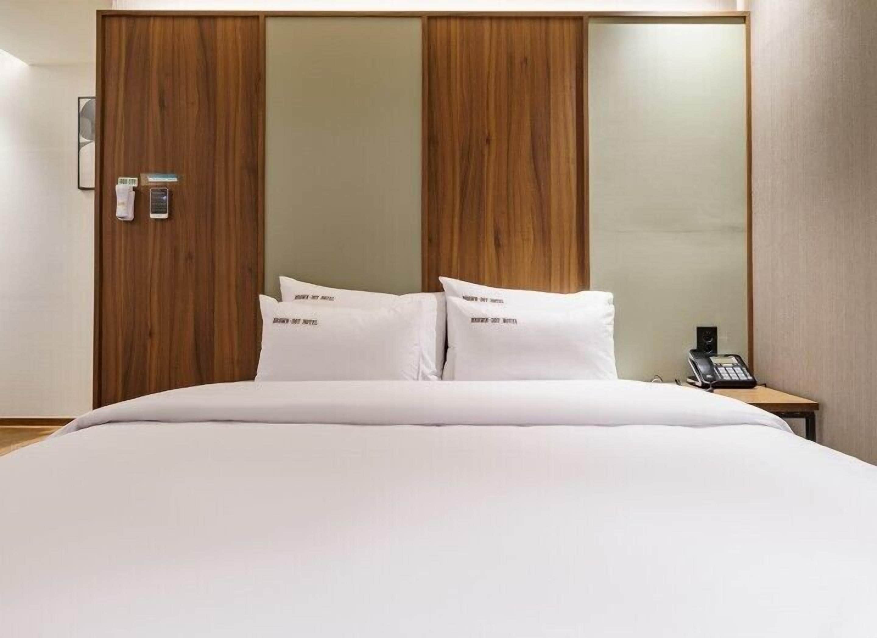 A hotel room with a large bed, wooden paneling on the walls, a bedside phone, and a small table with a lamp.