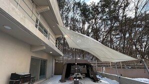 A covered outdoor patio with a grill and picnic table, surrounded by snow and trees. - Brown Dot Hotel Eurwangri (Incheon)