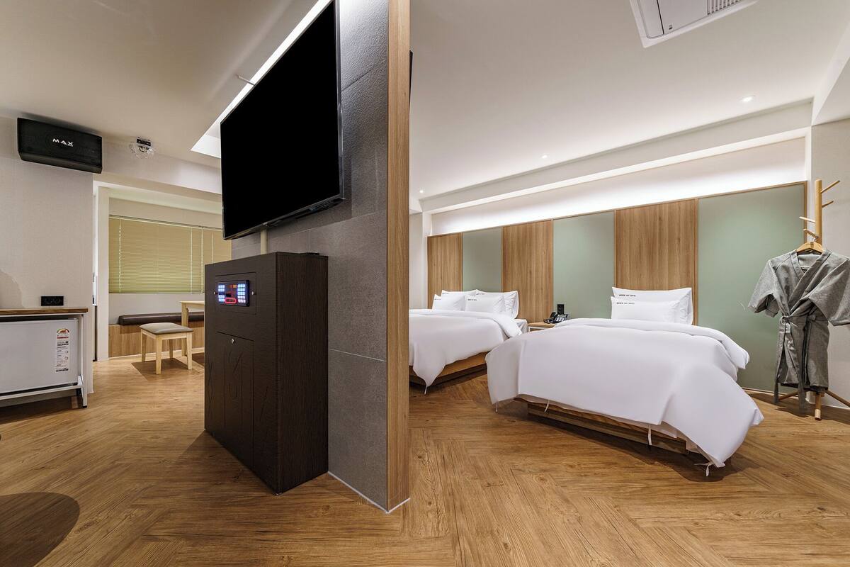 A hotel room with two beds, a TV, a minibar, and a wooden floor.
