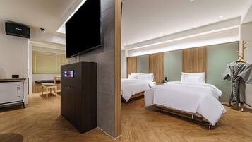 A hotel room with two beds, a TV, a minibar, and a wooden floor.