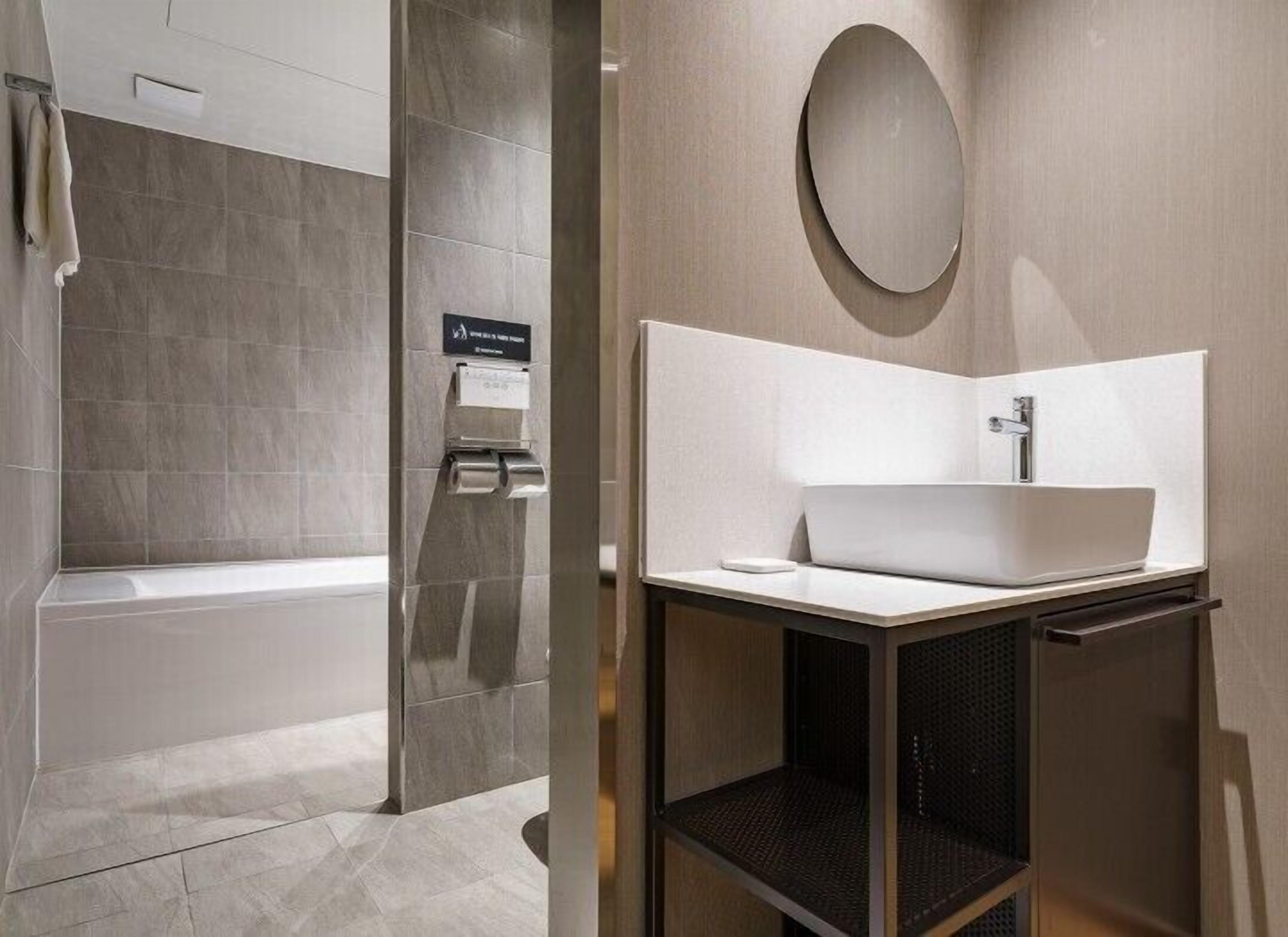 Un baño moderno con bañera, lavamanos con espejo y un perchero para toallas.