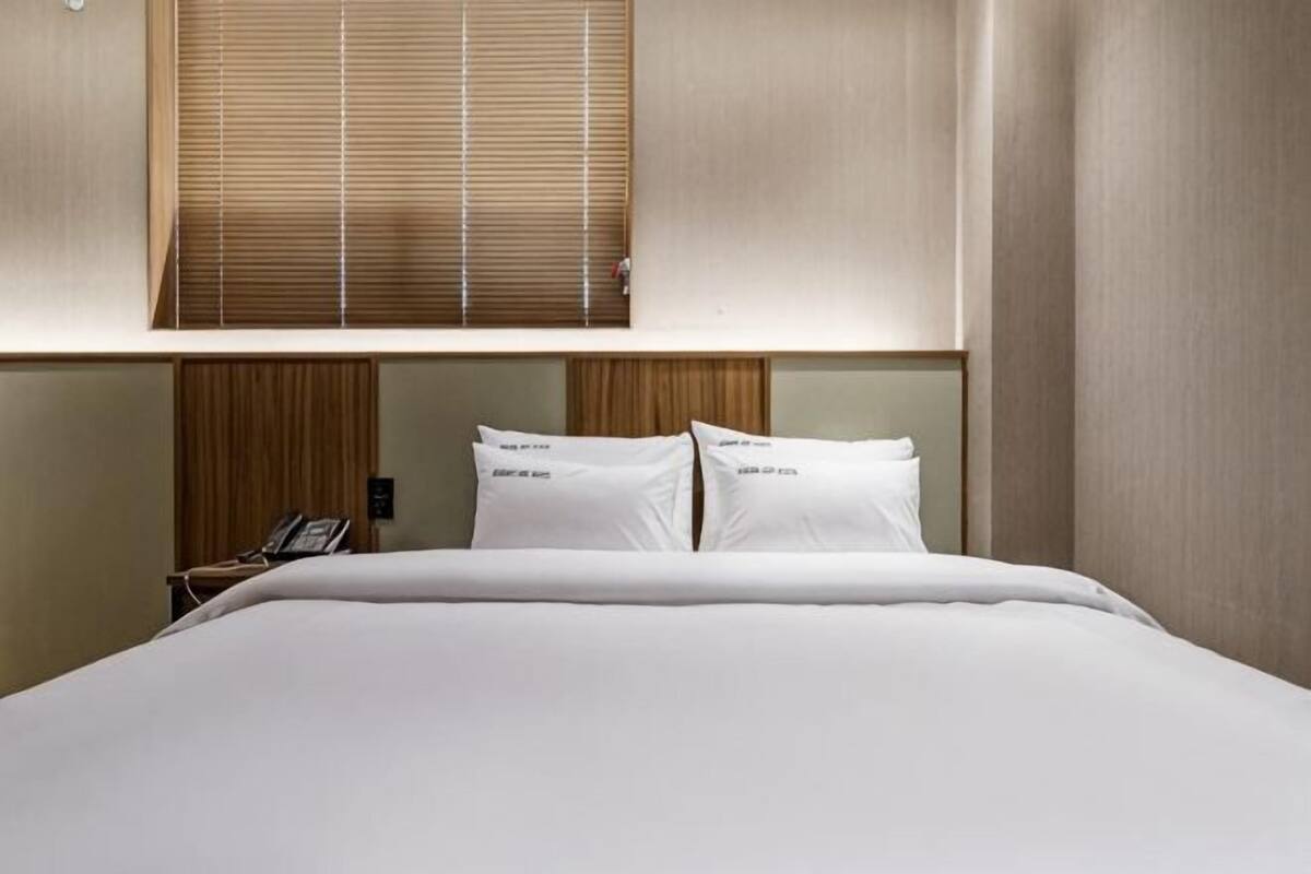 A hotel room with a bed, a telephone, and a window with blinds.