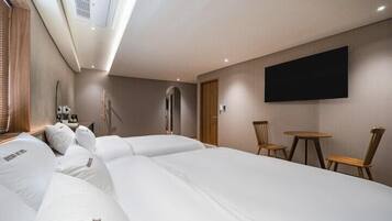 A hotel room with three beds, a TV, a small table, and a chair.