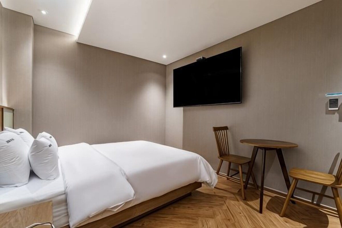 A hotel room with a bed, a TV mounted on the wall, a small round table, and two chairs.