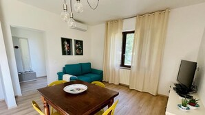 A dining area with a wooden table and yellow chairs, a teal sofa, and a TV on a cabinet. - Apartment The Limits (San Giuliano Terme)