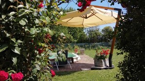 A garden with a pergola covered by a beige canopy, surrounded by lush greenery and vibrant red flowers. - Apartment The Limits (San Giuliano Terme)