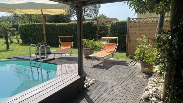 A wooden deck with a pool, two lounge chairs, and a pergola with a canopy. - Apartment The Limits (San Giuliano Terme)