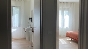 A room with a wooden floor, a bed with a pink bedspread, and a bathroom with a sink and mirror. - Apartment The Limits (San Giuliano Terme)