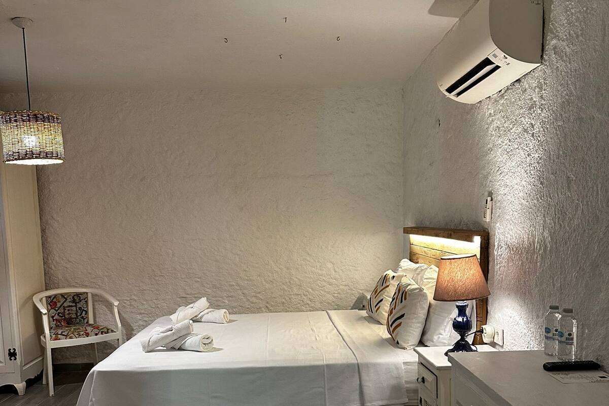 A bedroom with a bed, bedside table, chair, and a lamp.