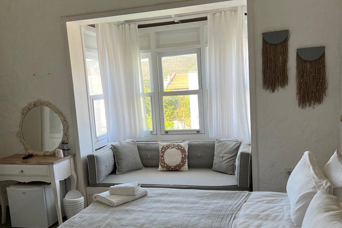 A bedroom with a bed, a bedside table, a mirror, a window with curtains, and wall decorations.