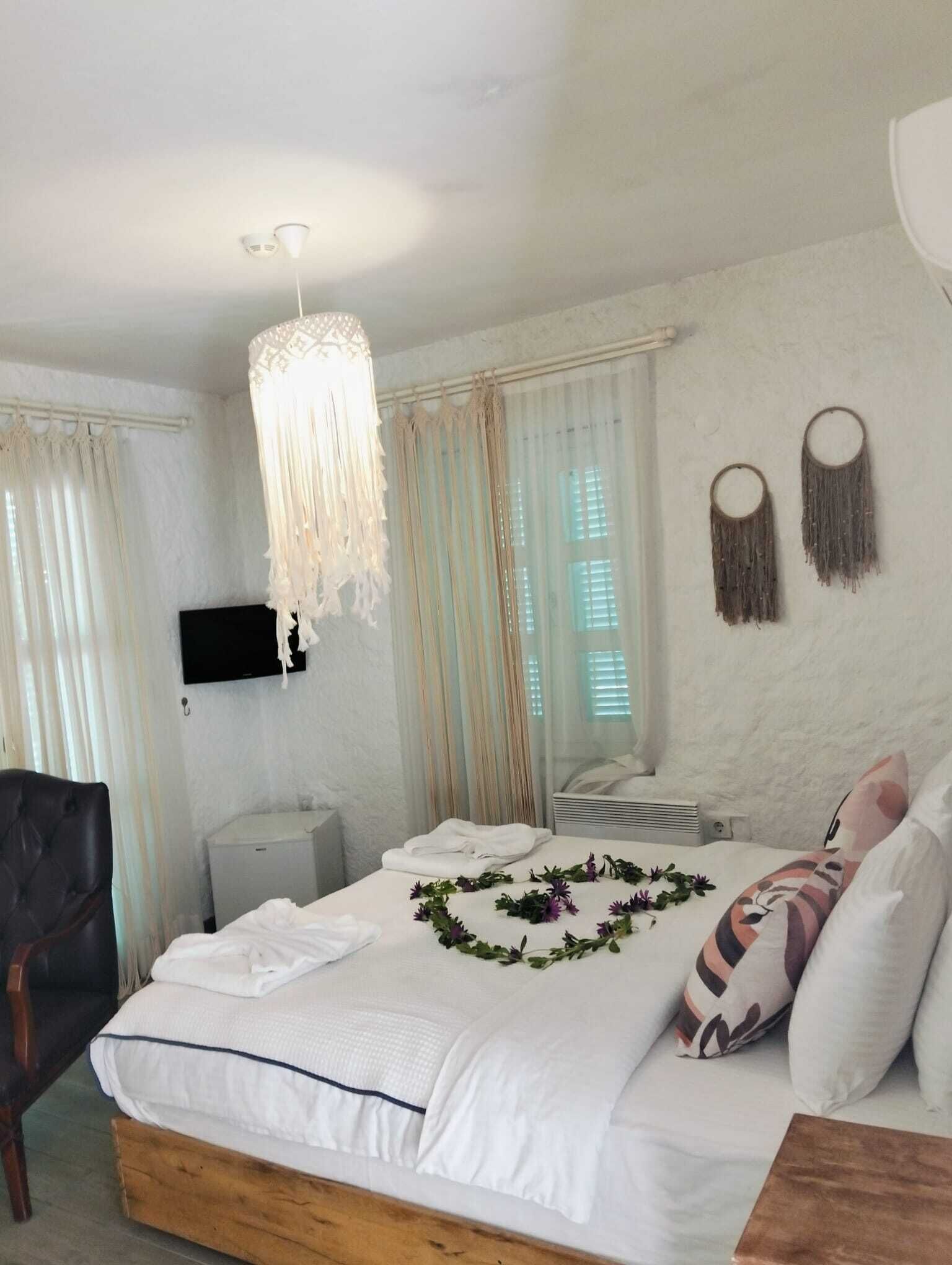 A bedroom with a bed, a chair, a bedside table, a hanging light fixture, and a wall-mounted TV.
