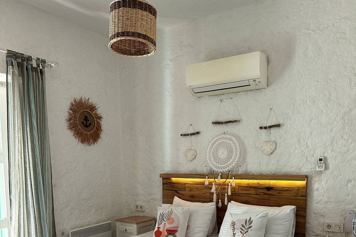 A bedroom with a wooden bed, white bedding, a hanging light fixture, a wall-mounted air conditioner, and decorative wall art.