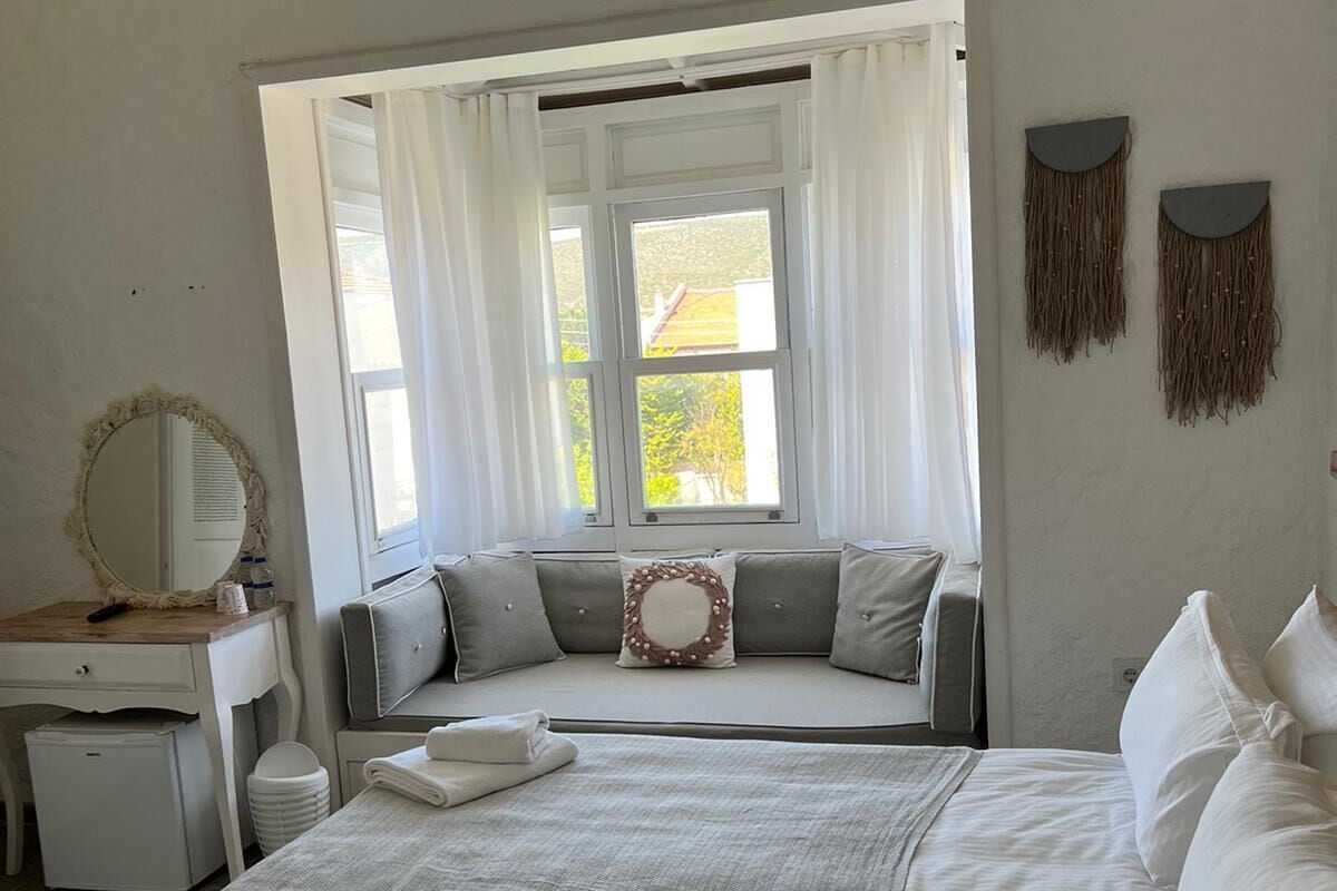 A bedroom with a bed, a bedside table, a mirror, a window with curtains, and wall decorations.