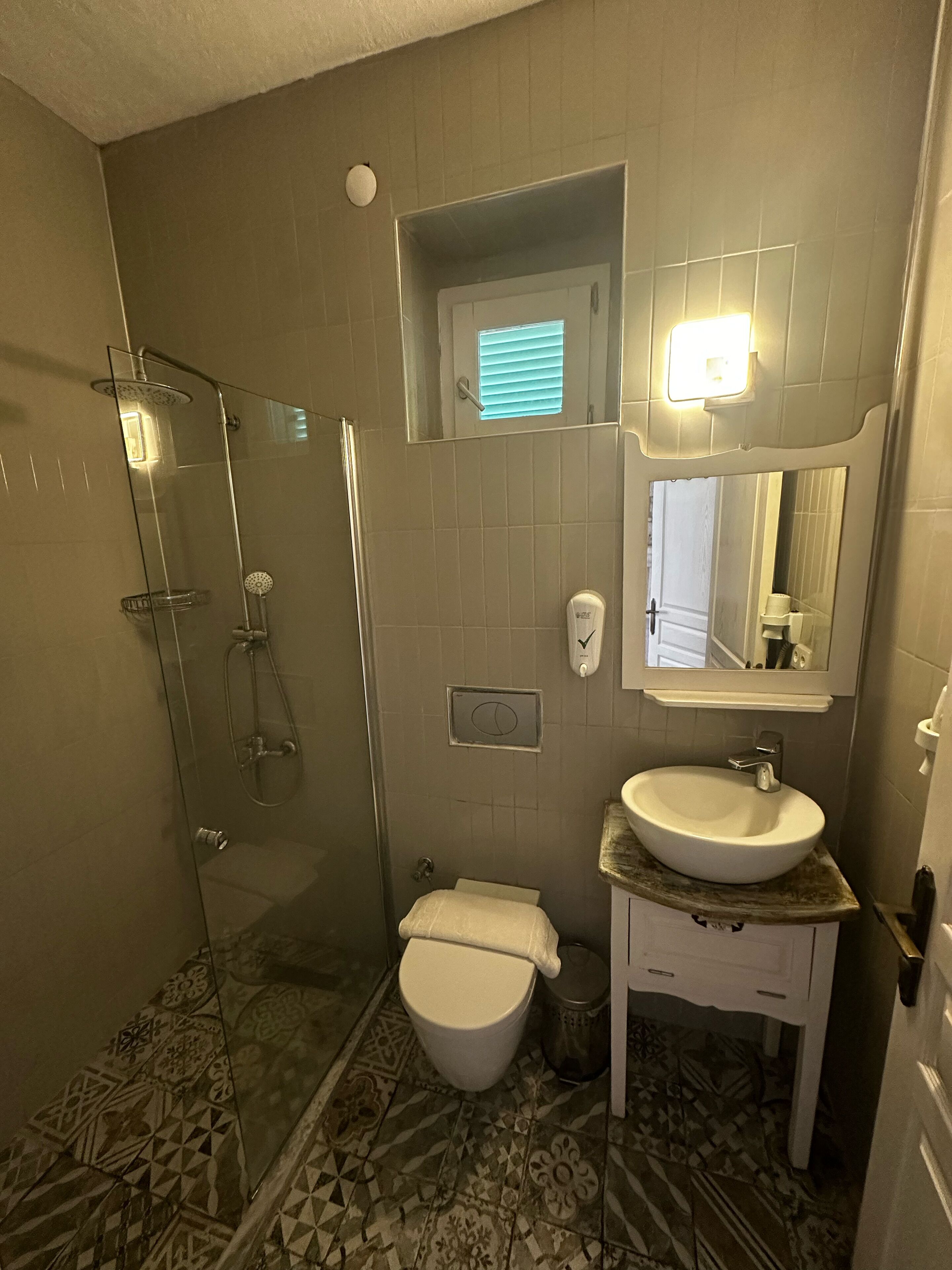 A bathroom with a glass shower enclosure, a toilet, a sink with a marble countertop, and a mirror above the sink.