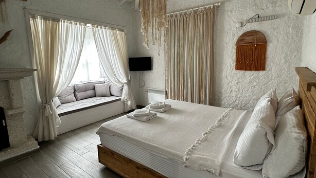 Un dormitorio con una cama grande, cabecera de madera, pared de piedra, ventana con cortinas y una lámpara colgante.