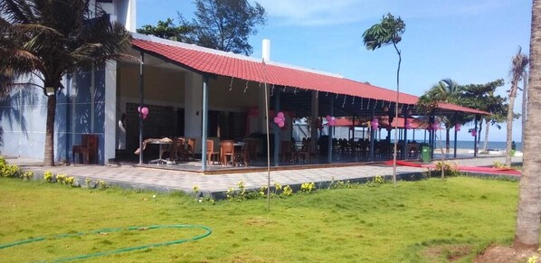 A building with a red roof and a covered outdoor area with tables and chairs. - Coral Beach Resort (Tirukalukundram)