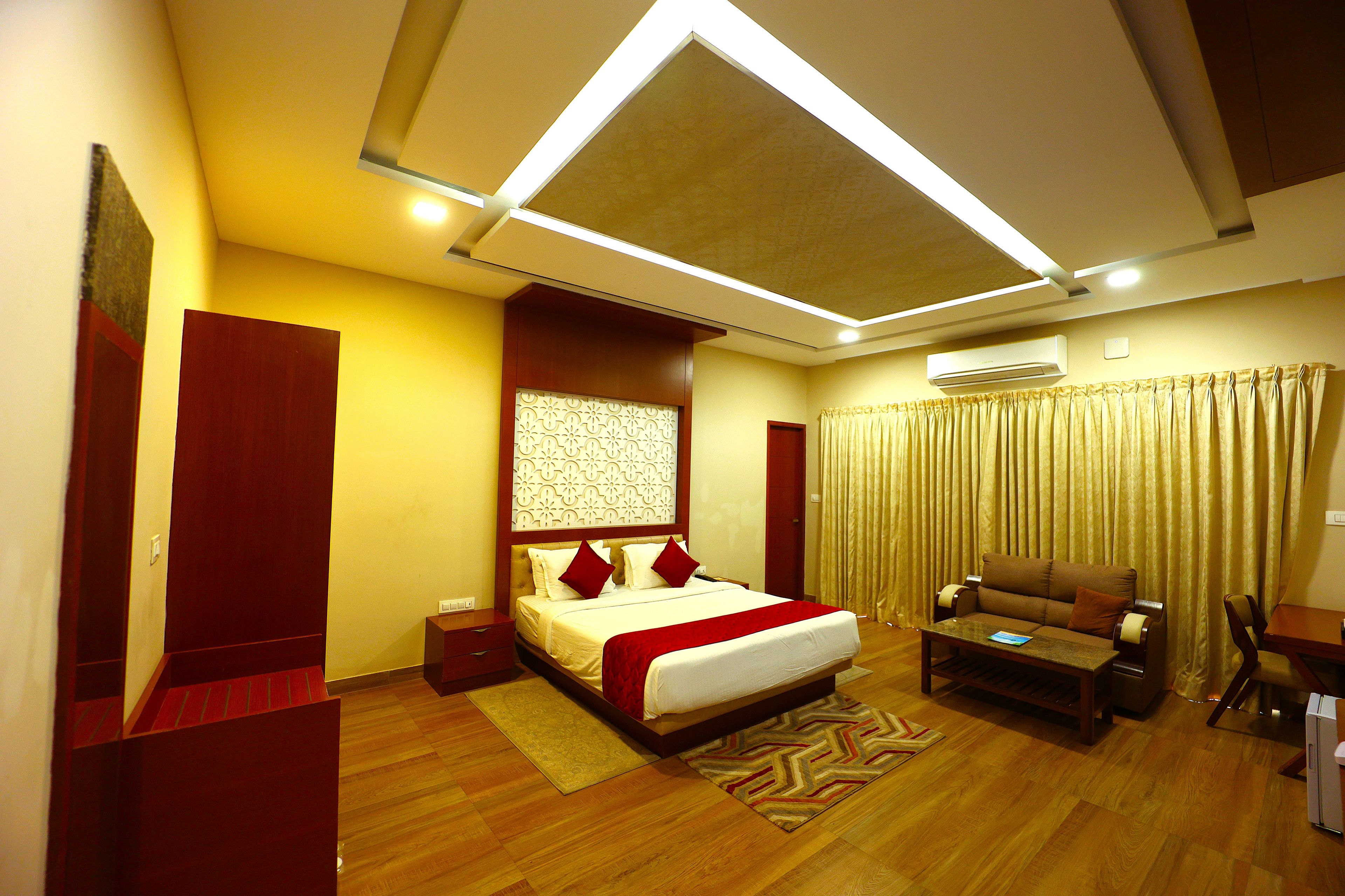 A hotel room with a bed, a sofa, a desk, and an air conditioning unit.