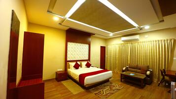 A hotel room with a bed, a sofa, a desk, and an air conditioning unit.