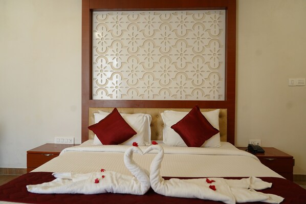 A hotel room with a large bed, two red pillows, a wooden headboard, and a decorative panel above the bed. - Coral Beach Resort (Tirukalukundram)