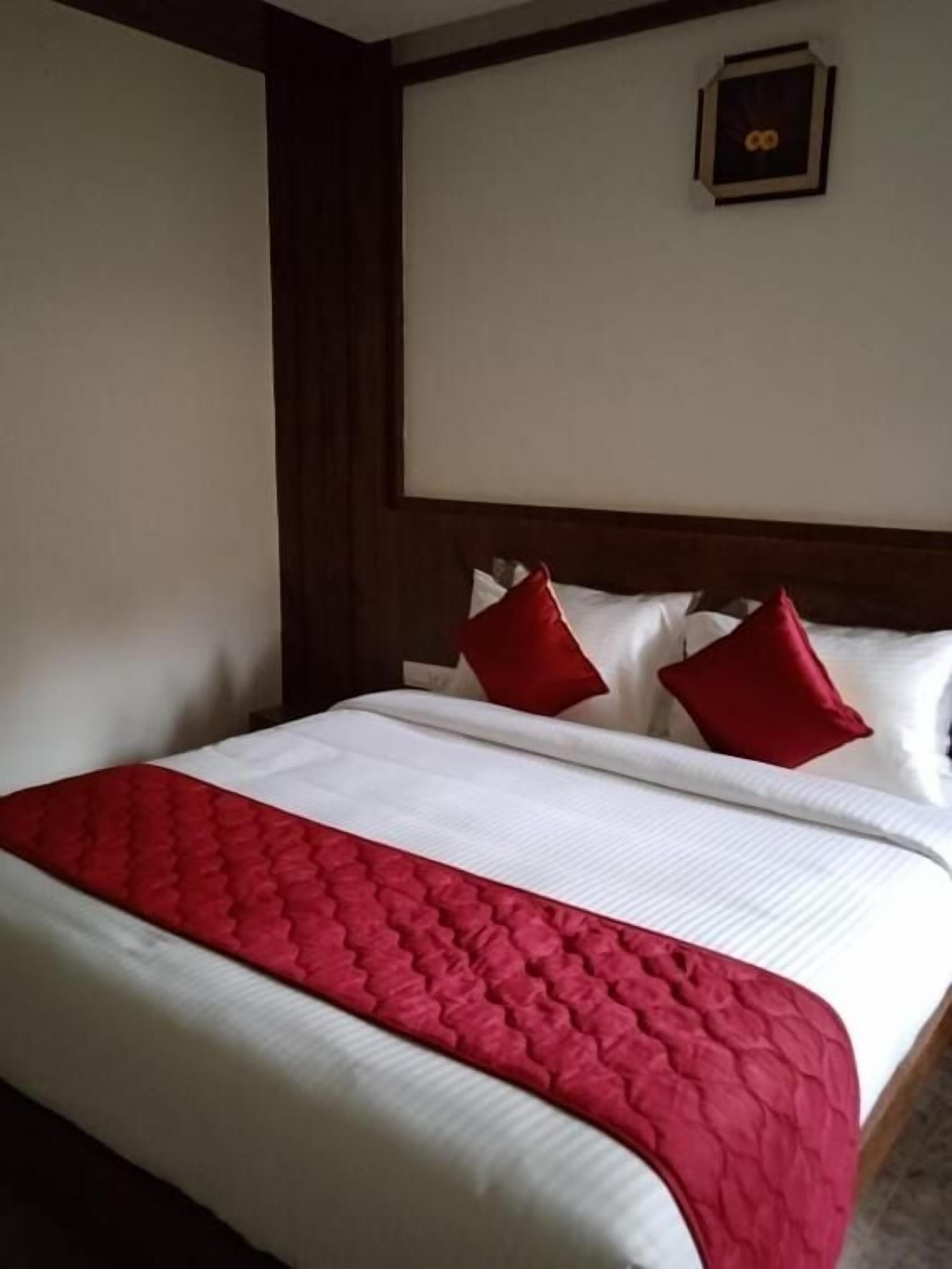 Una cama bien tendida con una colcha roja y blanca, un cabecero de madera y almohadas rojas.