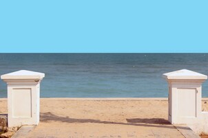 A beach with two white pillars and a sandy path leading to the sea.