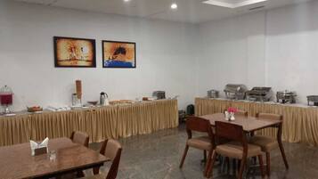 A conference room with tables and chairs, buffet setup, and two paintings on the wall.