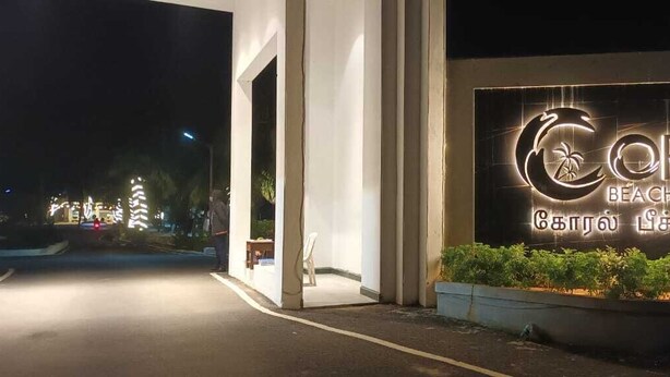 A sign for Coral Beach Resort with a palm tree logo, surrounded by greenery and a well-lit entrance. - Coral Beach Resort (Tirukalukundram)