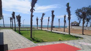A beachside walkway with palm trees, a red carpet, and a gazebo in the background. - Coral Beach Resort (Tirukalukundram)