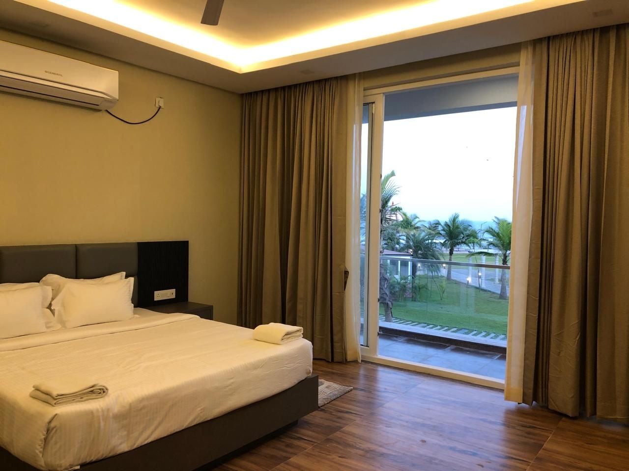 Ein Hotelzimmer mit einem großen Bett, einem Nachttisch, einer Wand-Klimaanlage und einer Glastür, die auf einen Balkon führt.