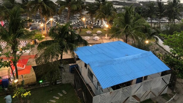 A beachside property with a blue-roofed building, palm trees, and a view of the ocean. - Sea Breeze Beach Resort (Murud)