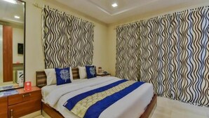 A hotel room with a large bed, a bedside table, a mirror, and curtains with a wavy pattern. - Sea Breeze Beach Resort (Murud)