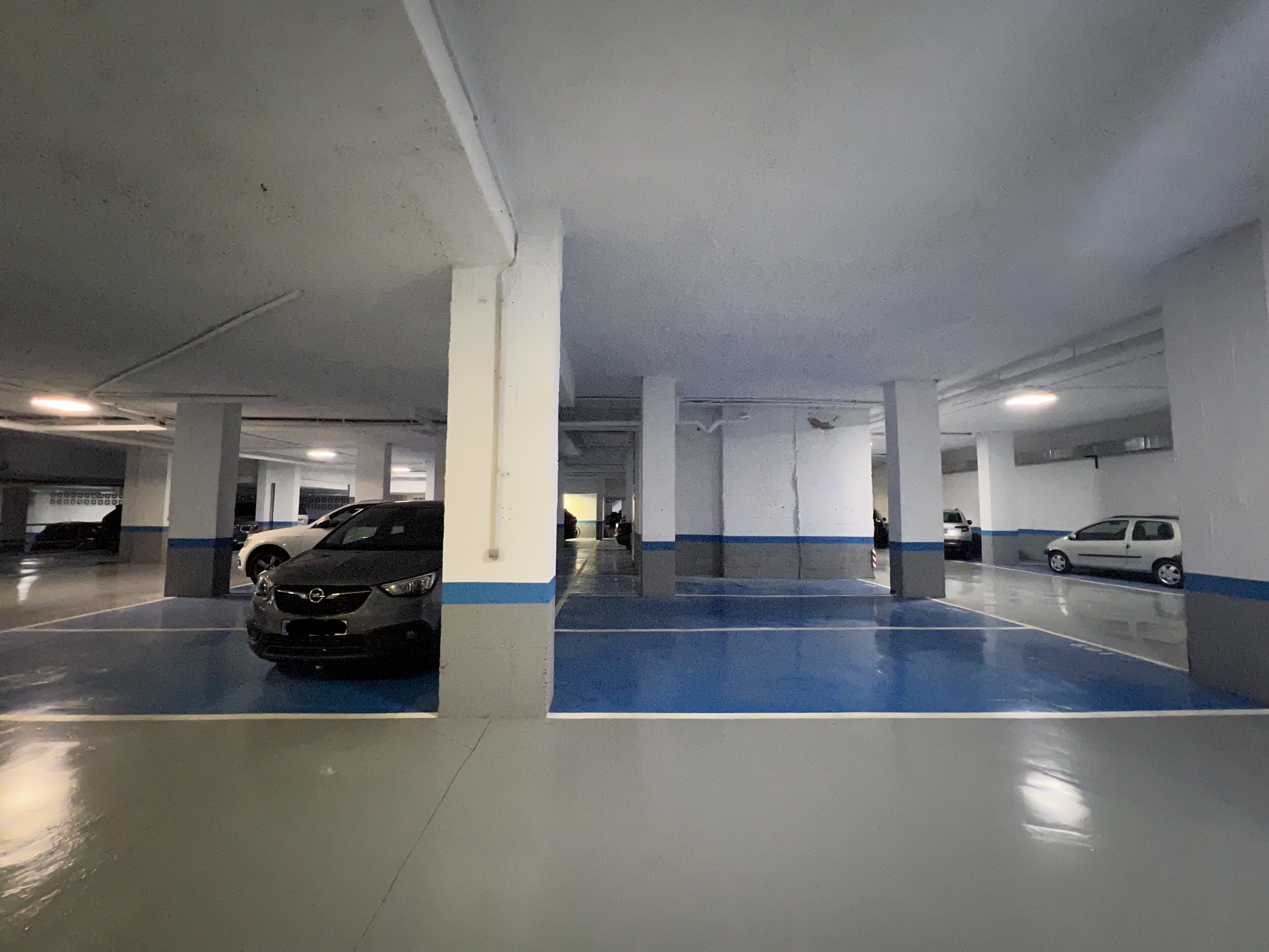 A multi-level parking garage with concrete pillars and blue-painted floor markings.