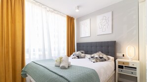 Un lit bien fait, avec une couverture verte et des oreillers, une table de chevet avec une lampe, et des œuvres d’art accrochées au mur.