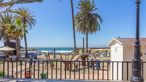 Une vue sur la plage, avec des palmiers, une terrasse en bois et un bâtiment portant l’inscription « MACELLIO ».