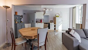 A modern kitchen with white cabinets, a dining table with chairs, and a sofa in a living area.