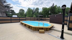 A rectangular wooden swimming pool with a ladder, surrounded by a gravel patio and a wooden fence.
