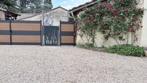 A gated entrance with a gravel driveway, a wooden fence, and a wall with climbing roses.