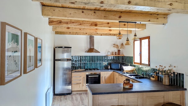 A kitchen with wooden beams, a stainless steel refrigerator, a stove, and a large island with stools. - COMFORTABLE CHALET - QUIET AND CLOSE TO EVERYTHING (Colmars)