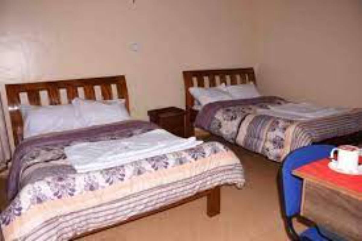 Ein Zimmer mit zwei Betten, jeweils mit einem hölzernen Kopfteil, einem kleinen Nachttisch und einem Sessel mit Tisch.