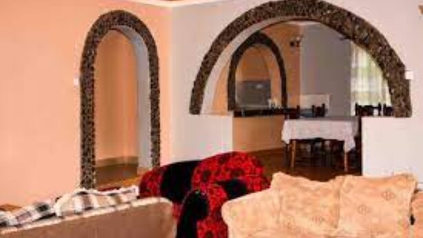A room with a sofa and a chair, a dining table with chairs, and a mirror with an arched frame.