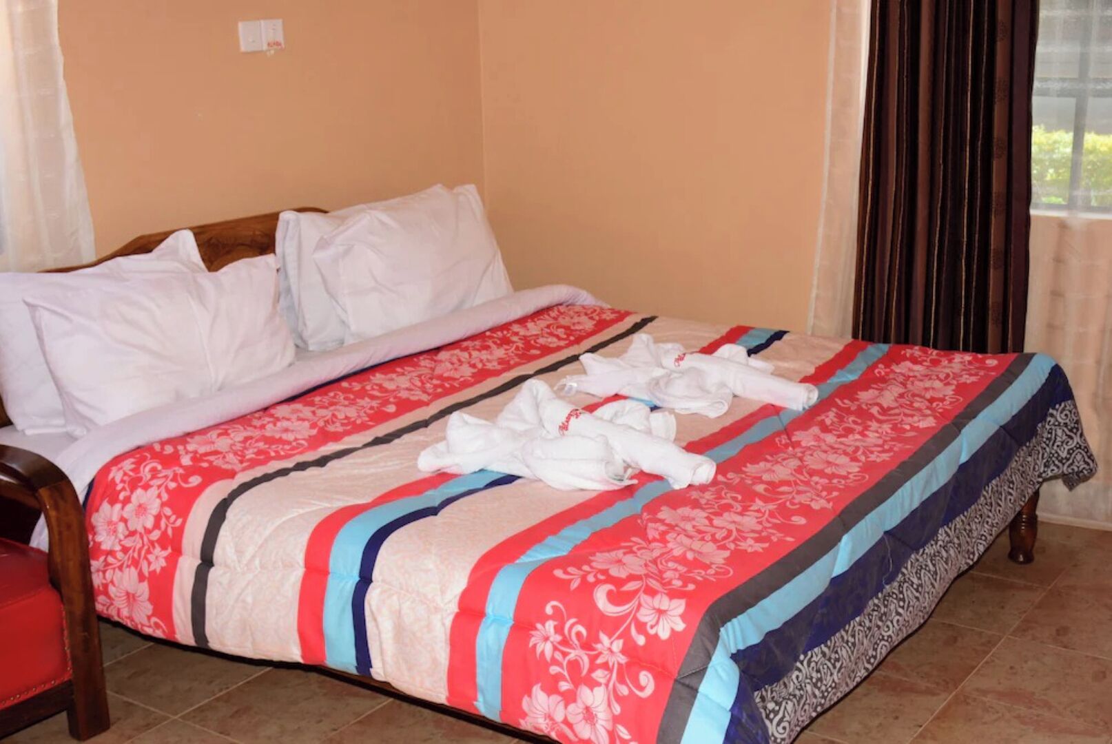 A hotel room with a bed, a wooden chair, and a window with curtains.