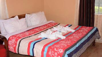 A hotel room with a bed, a wooden chair, and a window with curtains.