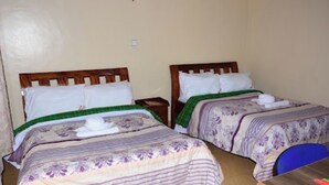 A room with two beds, each with a wooden headboard and white pillows. There is a small table with a chair and a blue cushion.