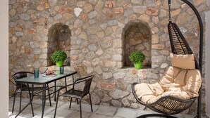 Zona salotto all'aperto con pareti in pietra, un tavolo, sedie e una poltrona sospesa.