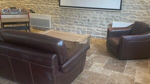 Ein gemütliches Wohnzimmer mit Steinwand, einem Kicker, einem großen Bildschirm und Ledersofas.